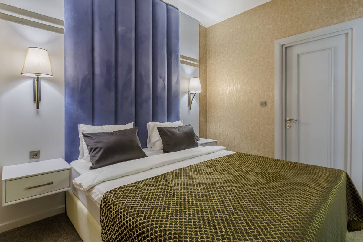 A hotel room with a bed, two bedside lamps, a nightstand, and a door.