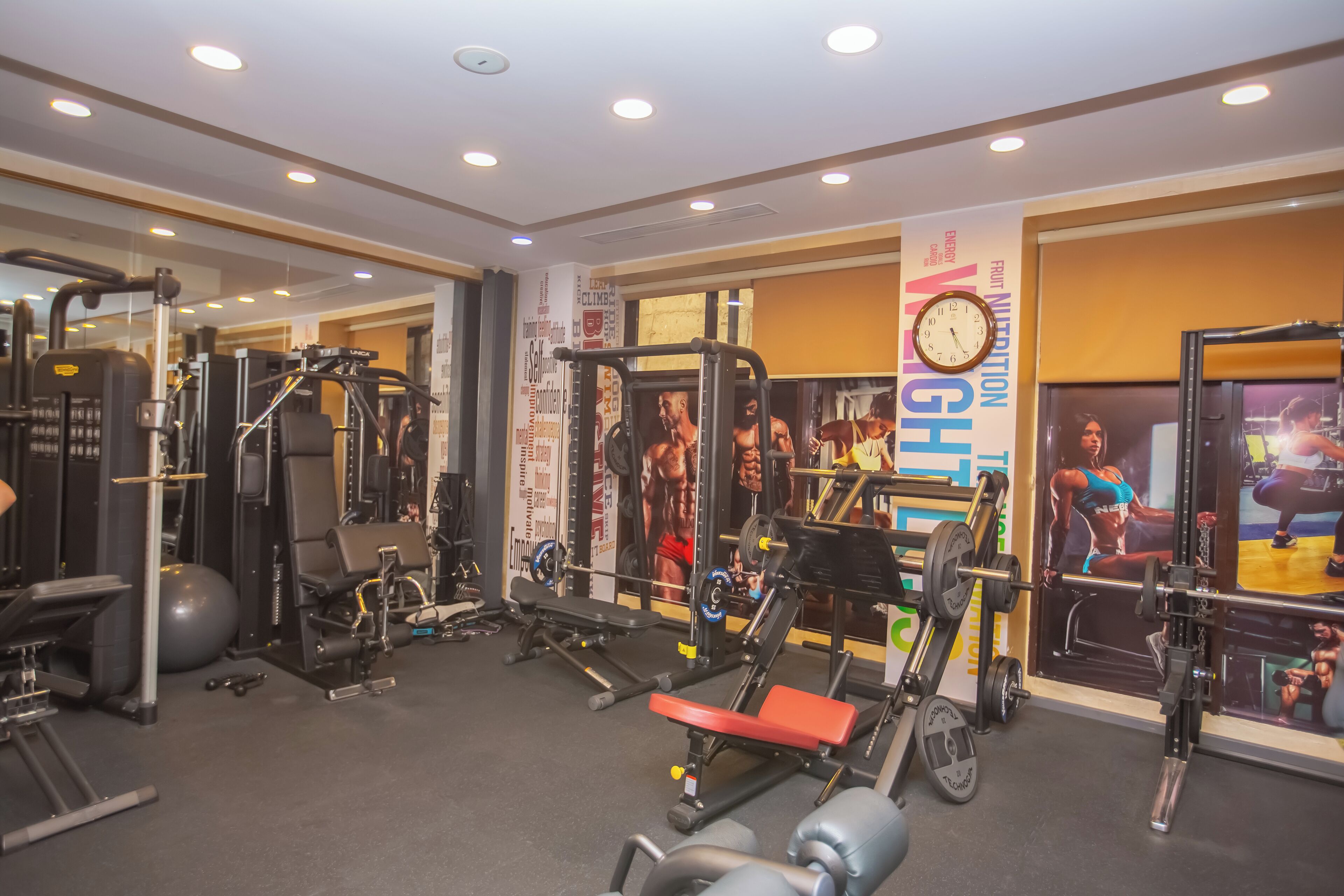 A gym with various exercise equipment, including weight machines and free weights, and motivational posters on the walls.