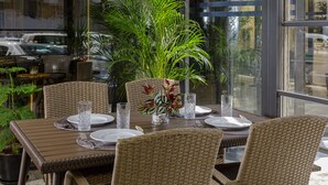 A dining area with wicker chairs, a glass table, and a potted plant. - Premium Park Hotel (Baku)