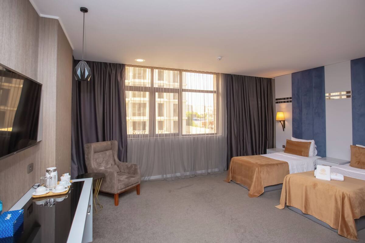 A hotel room with two beds, a desk with a chair, a TV, and a window with curtains.