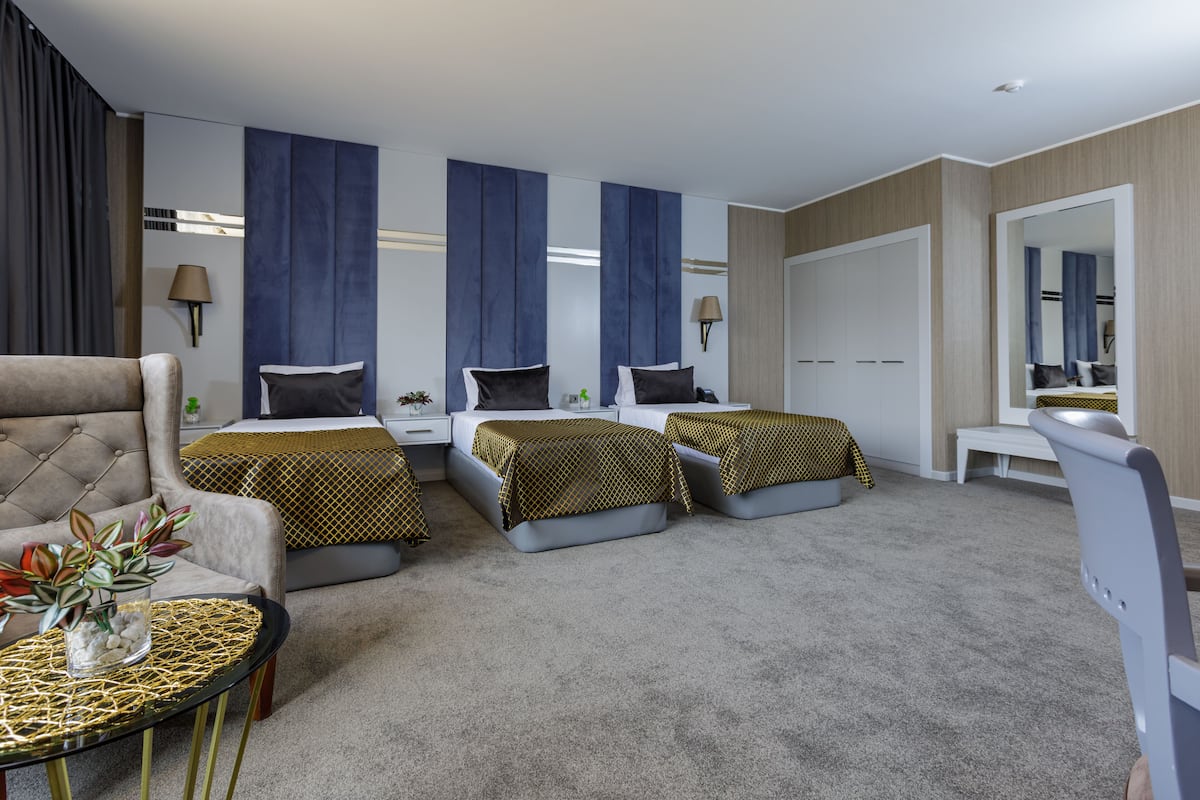 A modern hotel room with a sofa, two single beds, a small table, and a large mirror.