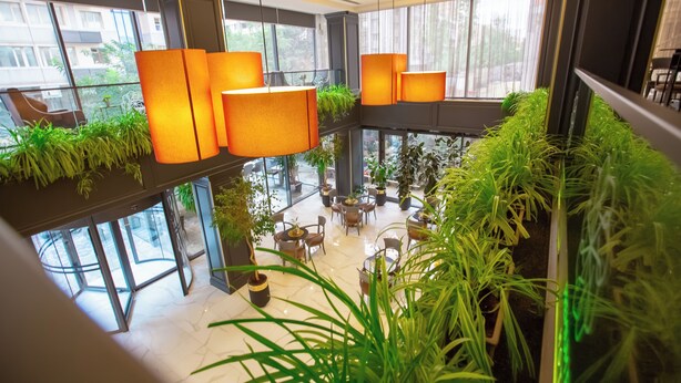 A modern indoor space with multiple levels, featuring potted plants, hanging lamps, and a variety of seating arrangements. - Premium Park Hotel (Baku)
