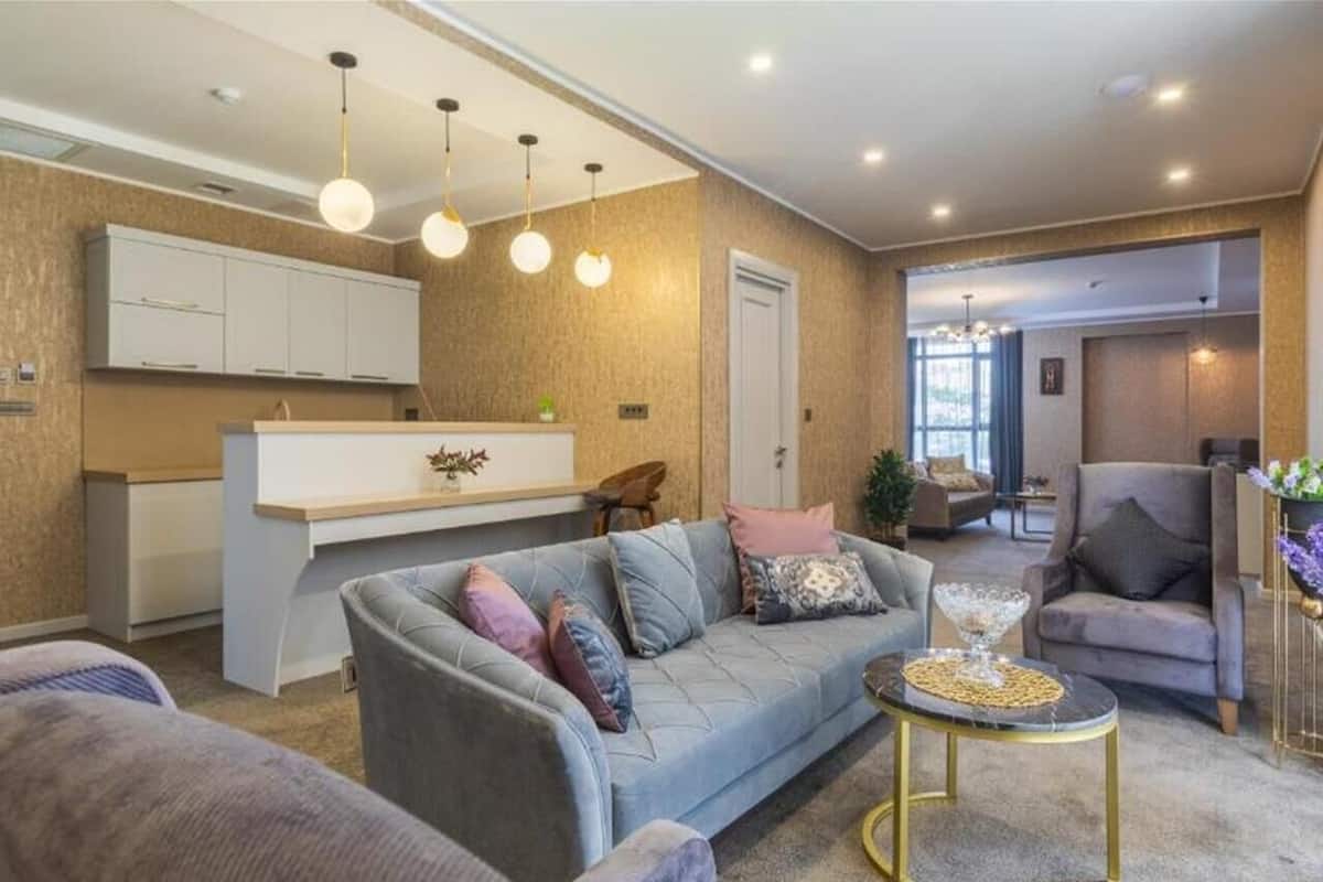 A modern living room with a grey sofa, a round coffee table, and a kitchen area in the background.