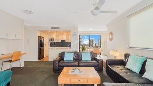 A modern living room with a sofa, coffee table, and a dining area with a view of the city. - Calypso Towers 901 - Coolangatta Beachfront - Min. 3 night stays! (Coolangatta)