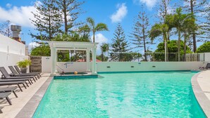 A swimming pool with lounge chairs, a small pavilion, and a view of trees and a building in the background. - Calypso Towers 901 - Coolangatta Beachfront - Min. 3 night stays! (Coolangatta)