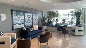 A modern lobby with a blue sofa, white armchairs, and a large abstract painting. - Calypso Towers 901 - Coolangatta Beachfront - Min. 3 night stays! (Coolangatta)