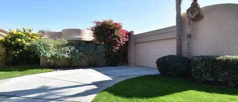 A residential driveway with a well-maintained lawn, a palm tree, and a house with a beige exterior.