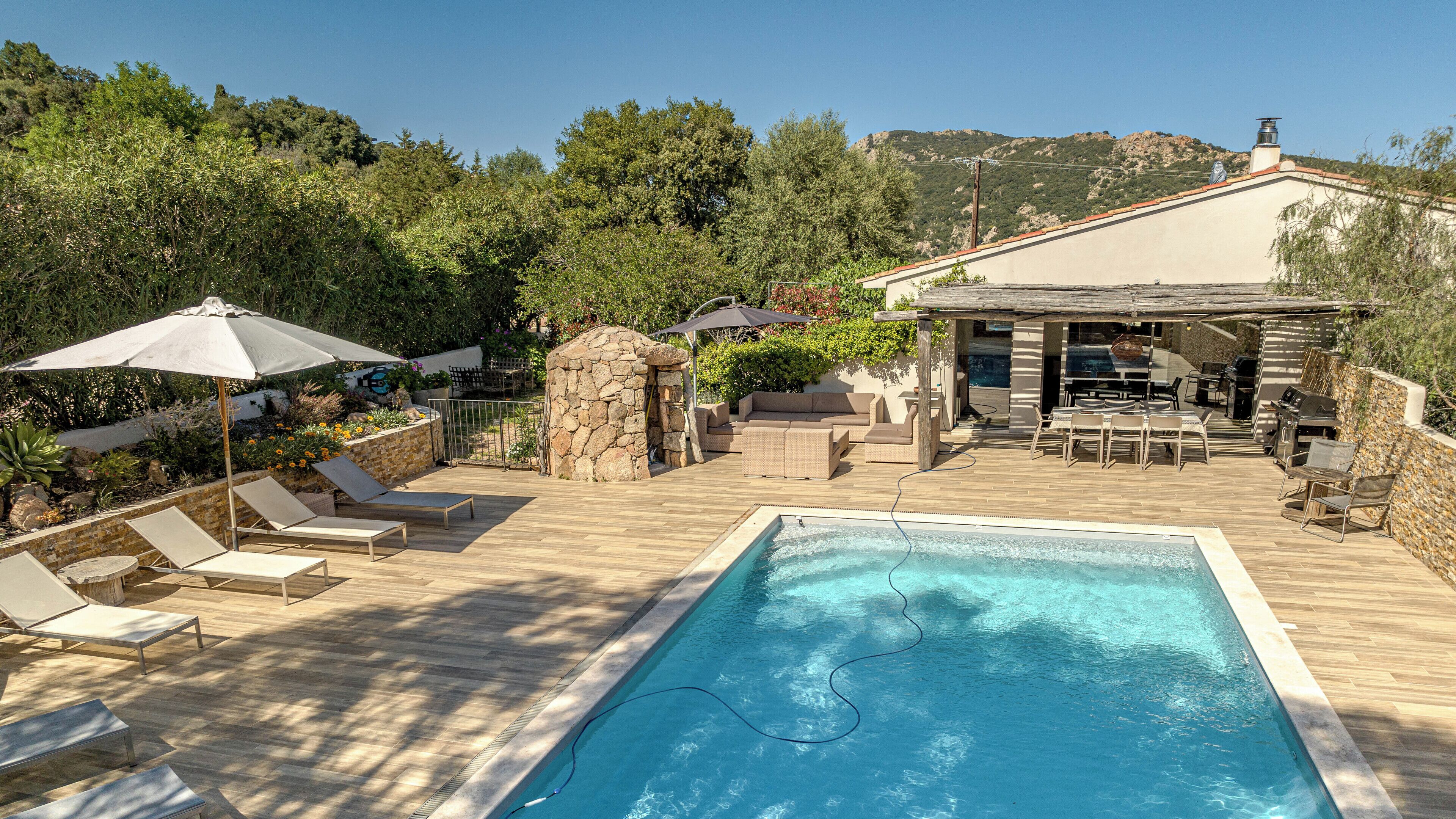 Area piscina con lettini, barbecue e un muro in pietra.