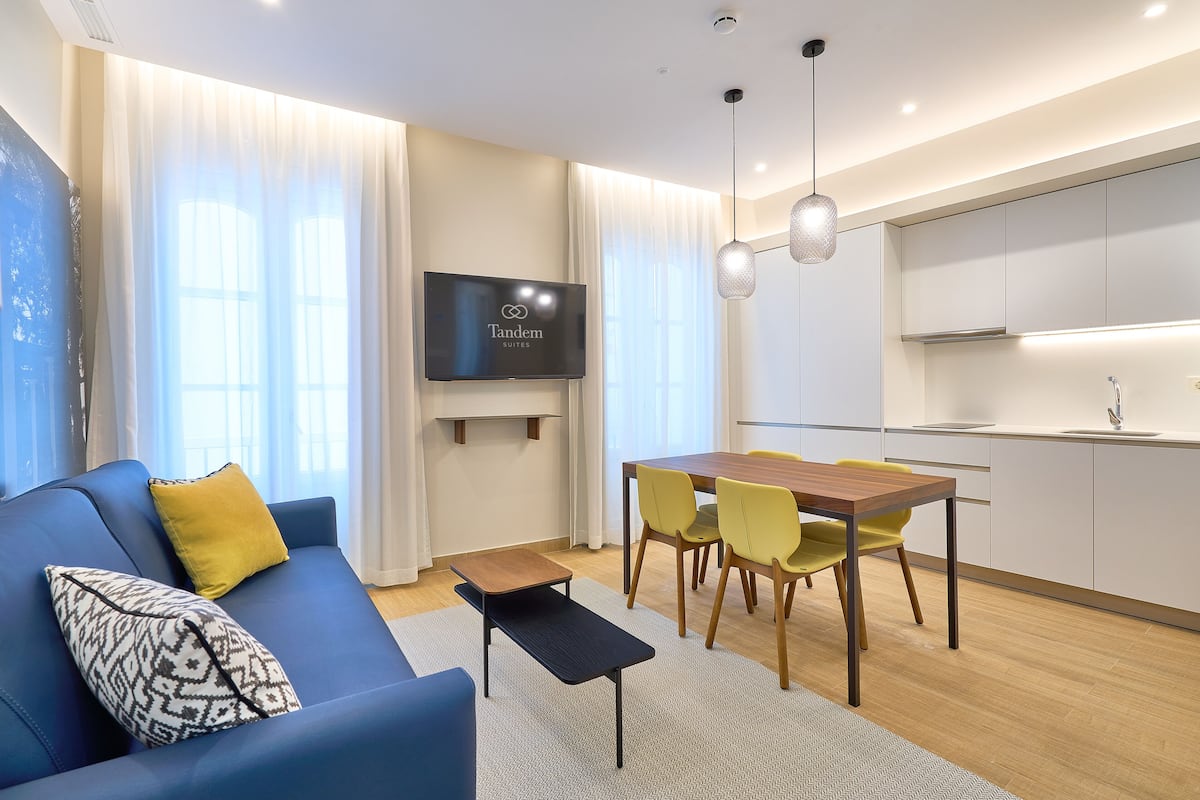 A modern living room with a sofa, a coffee table, a TV, and a dining area with chairs and a table.
