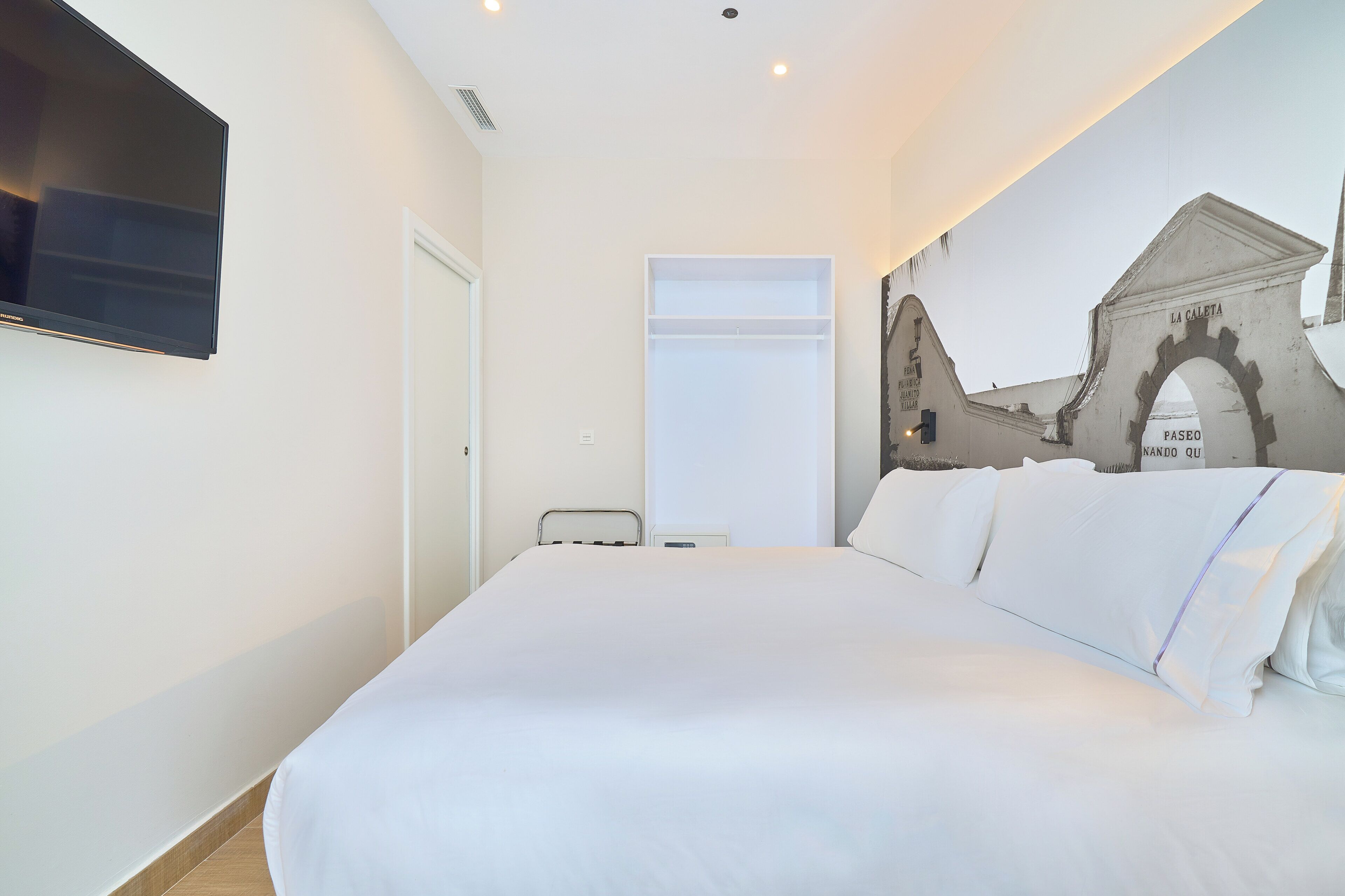 Un dormitorio con cama, un televisor de pantalla plana en la pared y un mural de un edificio.