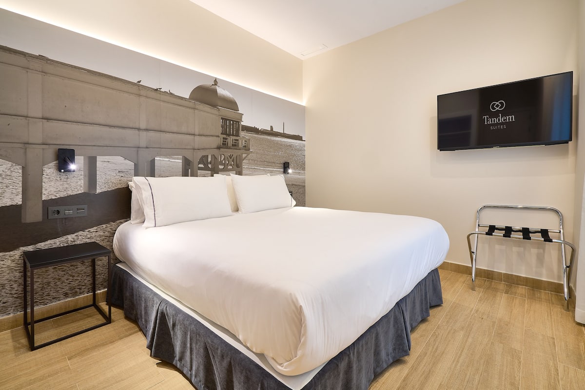 A hotel room with a large bed, a mounted TV, a wall-mounted phone, and a towel rack.