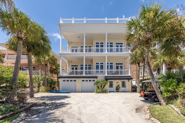 A two-story building with a balcony, surrounded by palm trees and a gravel driveway. - Beachview 913 - Oceanfront - St. Simons Island, GA (St. Simons Island)
