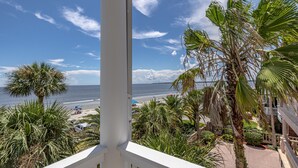 Uma varanda com vista para uma praia, palmeiras e céu claro.