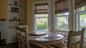 A dining area with a round table, white chairs, and a view of greenery outside. - Original Craftsman Cottage, at Magnolia Court Suites (Beaufort)