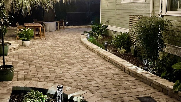 A paved patio area with a curved walkway, outdoor furniture, and string lights. - Original Craftsman Cottage, at Magnolia Court Suites (Beaufort)