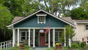 A two-story house with a green exterior, a front porch with white columns, and an American flag. - Original Craftsman Cottage, at Magnolia Court Suites (Beaufort)