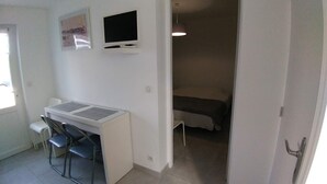 A small, compact room with a desk and two chairs, a bed, a television, and a door leading to another room. - New 2-room apartment in family home 100 m from beach and port (Capbreton)