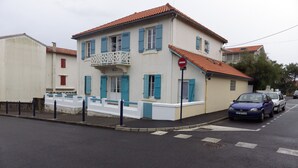 A two-story building with a balcony, a 'no entry' sign, and parked cars on the street. - New 2-room apartment in family home 100 m from beach and port (Capbreton)