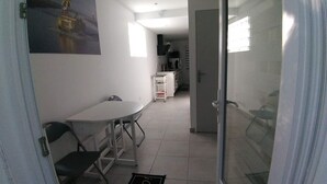 A narrow corridor with a white table and chairs, a kitchenette in the background, and a glass door leading to another room. - New 2-room apartment in family home 100 m from beach and port (Capbreton)