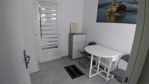 A small room with a white door, a white table, a chair, a cabinet, and a doormat. - New 2-room apartment in family home 100 m from beach and port (Capbreton)