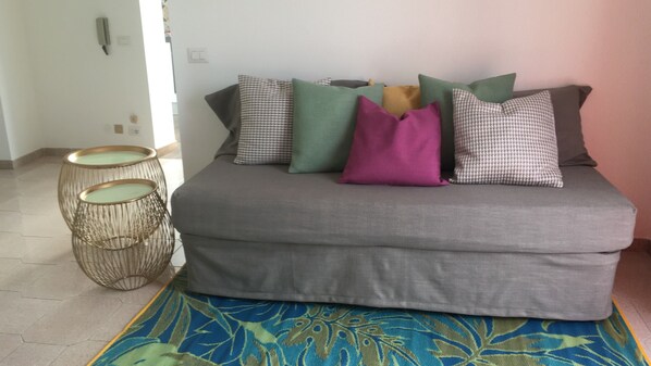 A grey sofa with multiple cushions in various colors, a patterned rug, and two round, woven side tables. - Beautiful house in Sicily, with an Amazing views and big spaces. (Capo d’orlando)