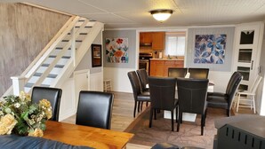 Amplia sala de estar con una mesa de comedor de madera, sillas de cuero negro, una escalera y una cocina al fondo.