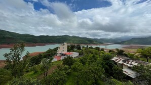 A view of a mountainous landscape with a body of water, a building with a red roof, and lush greenery. - CosmicStays Countryside Panorama-Lakeview Bungalow (Paud)