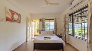 A bedroom with a bed, a nightstand, a window with curtains, a ceiling fan, and an air conditioning unit. - CosmicStays Countryside Panorama-Lakeview Bungalow (Paud)
