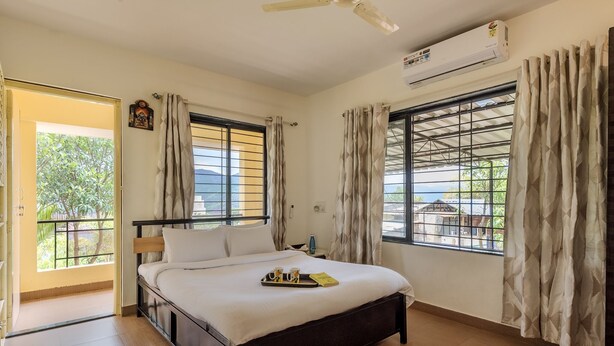 A hotel room with a bed, a ceiling fan, an air conditioner, and windows with curtains. - CosmicStays Countryside Panorama-Lakeview Bungalow (Paud)