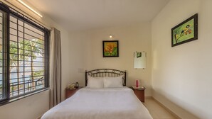 A neatly made bed in a room with a large window, a painting on the wall, and a small table with a lamp. - CosmicStays Countryside Panorama-Lakeview Bungalow (Paud)