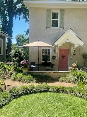 A house with a red door, a small porch with a table and chairs, and a large umbrella.
