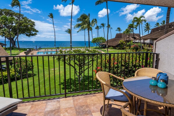 Un balcon avec vue sur l’océan et les palmiers, une piscine et du mobilier d’extérieur.