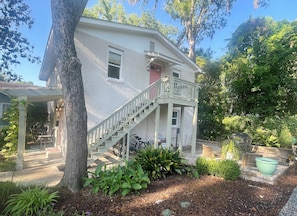 A two-story house with a covered porch, a staircase, and a garden with various plants. - Jasmine Suite #3, at Magnolia Court Suites (Beaufort)