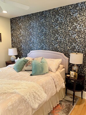 Une chambre à coucher avec un papier peint à motifs floraux, un lit avec une tête de lit blanche et deux tables de chevet avec des lampes.