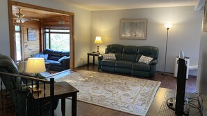 A living room with a dark green leather sofa, a wooden coffee table, a lamp, a TV, and a laptop on a desk. - Beautiful Home in Glendo (Glendo)