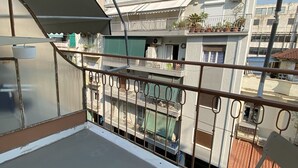 A balcony with a metal railing, a view of a multi-story building with balconies and satellite dishes, and a clear blue sky. - A Skip Away from the Acropolis Museum (Athens)