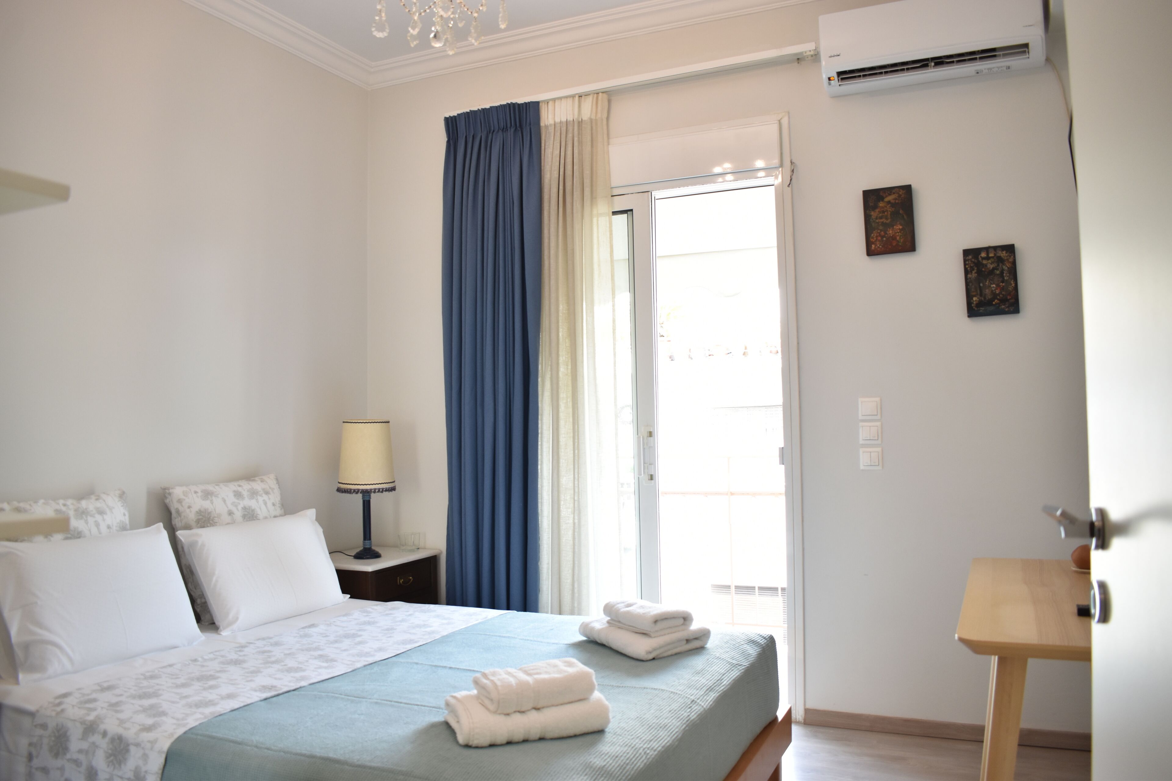 A hotel room with a bed, a nightstand, a lamp, a window with curtains, and a door.