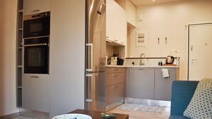 A compact kitchen with built-in appliances, a dining area with a table and a blue sofa, and a small rug on the floor. - A Skip Away from the Acropolis Museum (Athens)