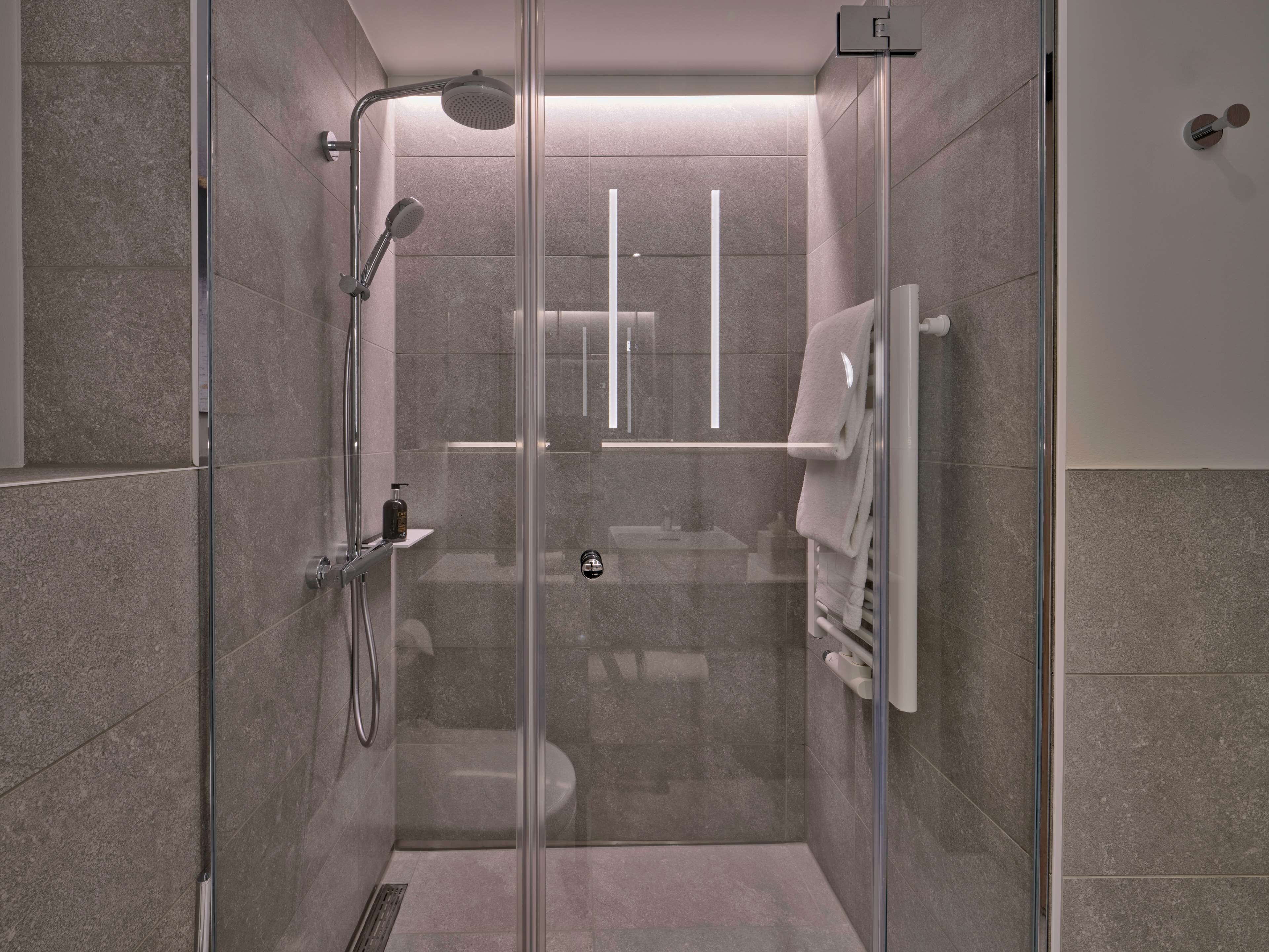 A modern shower with a glass door, a handheld showerhead, and a wall-mounted towel rack.
