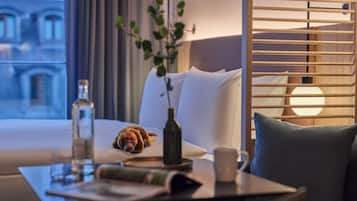 A hotel room with a bed, a bedside table with a bottle, a cup, and a plant.