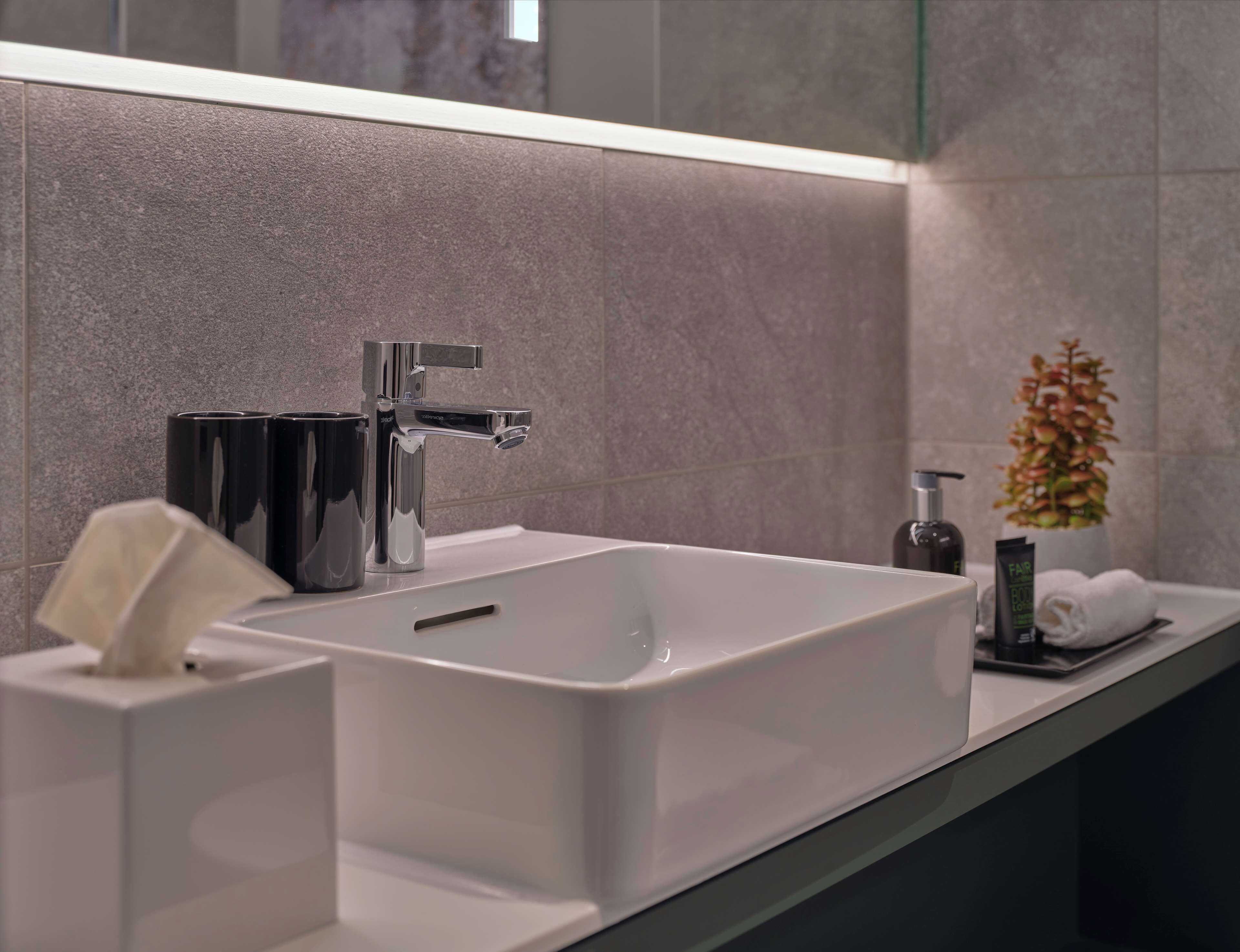 Ein modernes Badezimmer mit einem großen weißen Waschbecken, einem chromfarbenen Wasserhahn und einem Spiegel darüber.