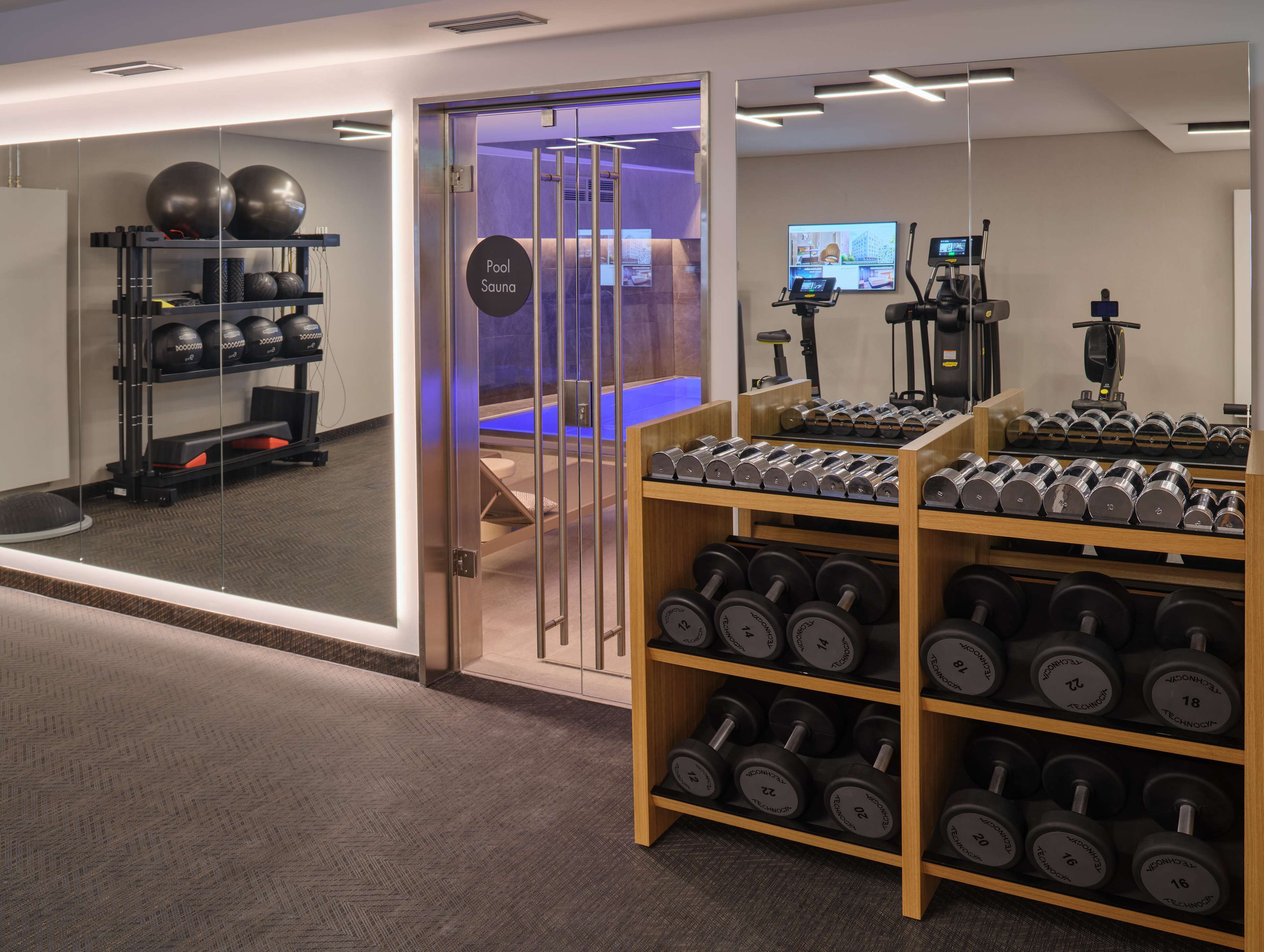 A gym with a pool sauna, exercise equipment, and a rack of dumbbells.