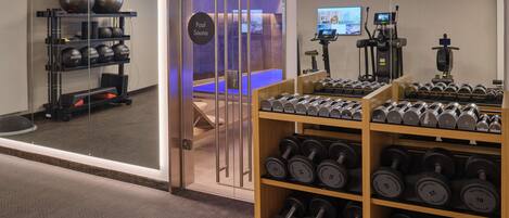 A gym with a pool sauna, exercise equipment, and a rack of dumbbells.