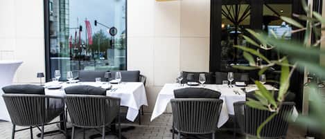 An outdoor dining area with tables and chairs, a yellow umbrella, and a view of the cityscape through large windows.