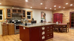A kitchen with wooden cabinets, a central island, and a dining area with wooden chairs. -  COZY BEAR LODGE - BEAUTIFUL MOUNTAIN GET AWAY (Island Park)