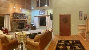 A cozy living room with a stone fireplace, leather sofa, and a large window with curtains. -  COZY BEAR LODGE - BEAUTIFUL MOUNTAIN GET AWAY (Island Park)