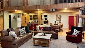 A spacious living area with a high ceiling, wooden flooring, and a kitchen in the background. -  COZY BEAR LODGE - BEAUTIFUL MOUNTAIN GET AWAY (Island Park)