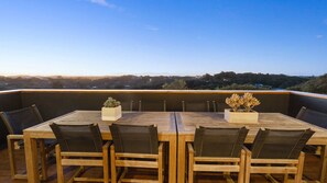 A wooden deck with a table and chairs, two potted plants, and a view of the landscape.