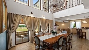 Un vaste espace dédié à la salle à manger, avec une longue table en bois, de nombreuses chaises et une vue sur l’extérieur.