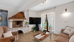 Un salon doté d’une cheminée, d’un téléviseur à écran plat, d’une table basse en bois et offrant une vue sur une piscine.